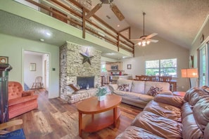 A spacious living room with a stone fireplace, leather sofas, and a high ceiling with exposed beams.