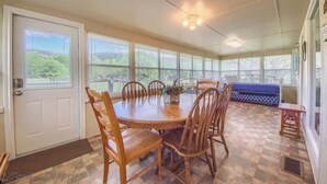 A covered dining area with a round table and chairs, a bench, and large windows with blinds. - RR 9084BC Bluebonnet Cabin (New Braunfels)