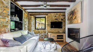 A cozy living room with a stone wall, a white sofa, a black chair, and a fireplace. - Charming gîte with SPA / Jacuzzi Lodge in the Basque Country (VALCARLOS)
