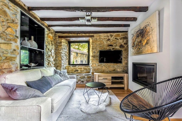 A cozy living room with a stone wall, a white sofa, a black chair, and a fireplace. - Charming gîte with SPA / Jacuzzi Lodge in the Basque Country (VALCARLOS)