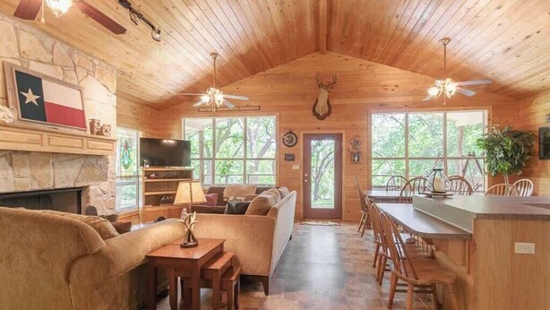 L’intérieur d’une cabane en rondins, avec une cheminée en pierre, un canapé, une table à manger et un coin cuisine.