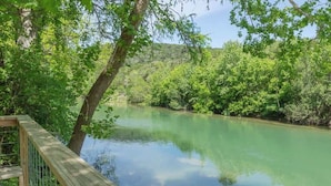 Une terrasse en bois surplombe une rivière paisible, bordée de chaque côté d’une végétation luxuriante.