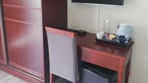 A room with a desk, a chair, a TV mounted on the wall, a small fridge, and a coffee maker on the desk. - Azinnia Rivonia Guest House (Sandton)