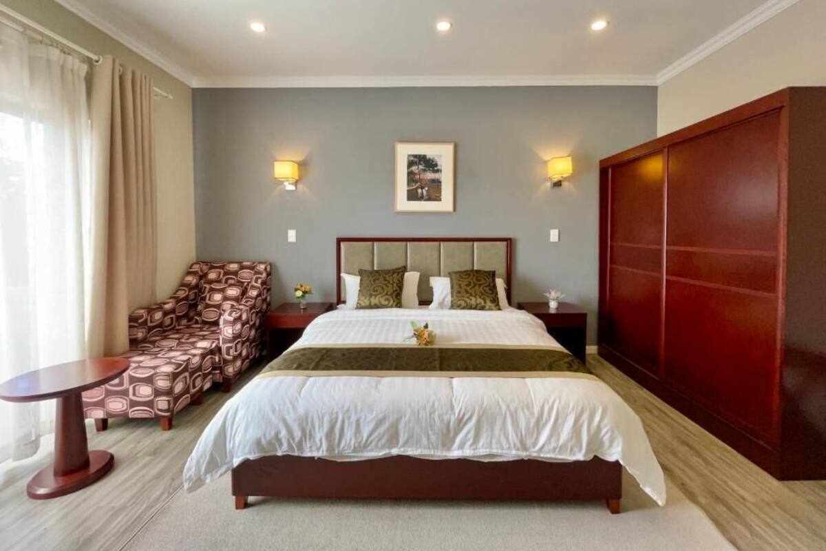 A hotel room with a large bed, a sofa, a small table, and a wardrobe.