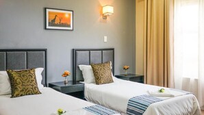 A hotel room with two beds, a nightstand with a lamp, a framed picture on the wall, and a window with curtains. - Azinnia Rivonia Guest House (Sandton)