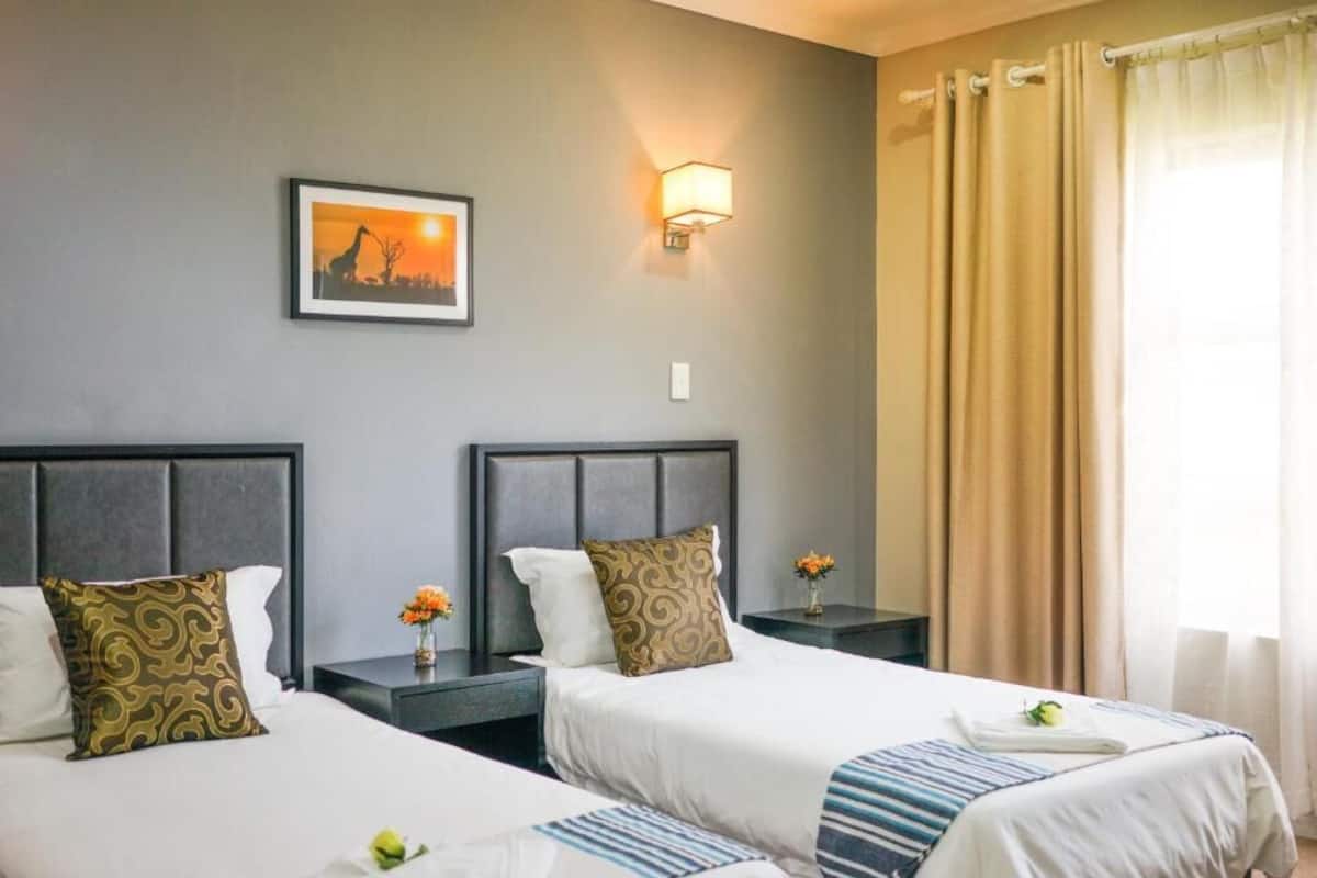 A hotel room with two beds, a nightstand with a lamp, a framed picture on the wall, and a window with curtains.