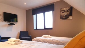 A hotel room with two beds, a flat-screen TV mounted on the wall, a window with blinds, and a painting on the wall. - Memories (Ghent)