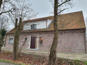 A brick building with a tiled roof, a central door, and two windows.