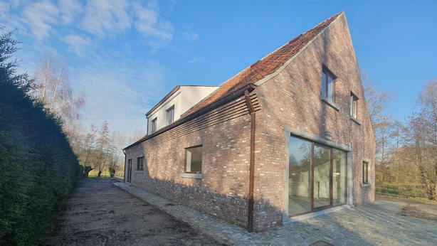 A modern house with a sloped roof, large windows, and a paved driveway. - Memories (Ghent)