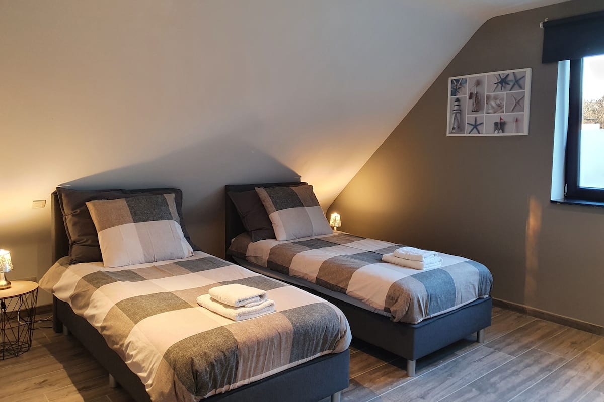 Un dormitorio con dos camas, una mesita pequeña y una estantería en la pared con objetos decorativos.