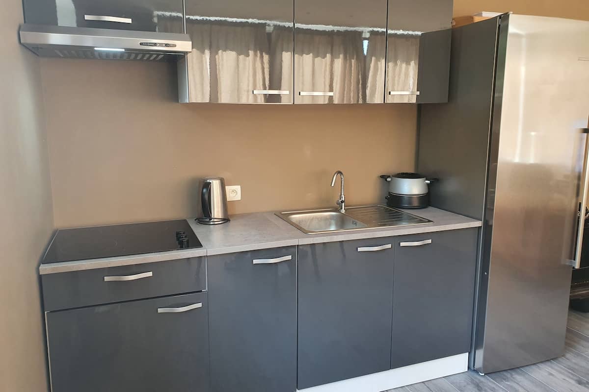 Una cocina moderna con un refrigerador de acero inoxidable, un horno empotrado, un lavamanos y una tetera.