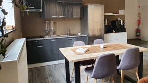 A modern kitchen with dark cabinets, a stainless steel refrigerator, a coffee machine, and a dining area with a wooden table and chairs. - Memories (Ghent)