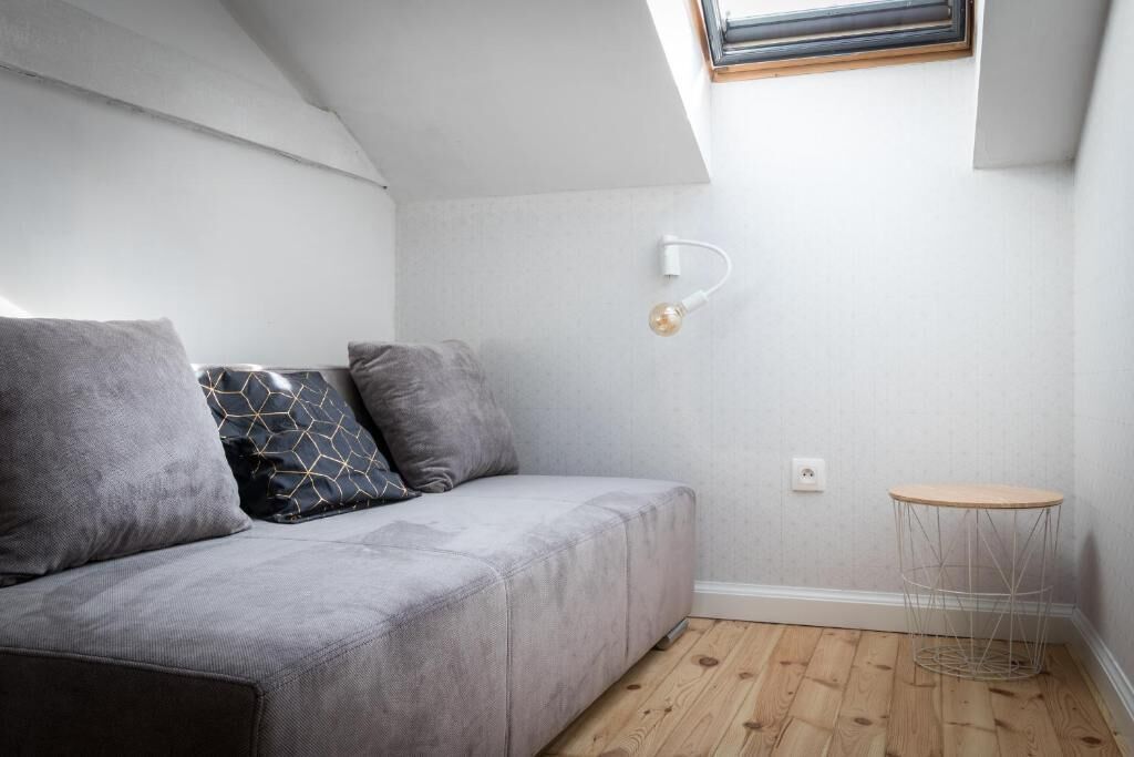 A modern, compact living space with a grey sofa, a small round table, and a slanted ceiling with a skylight.