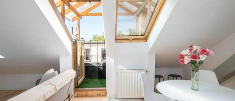 A small, modern room with a loft bed, a dining table, and a large skylight.