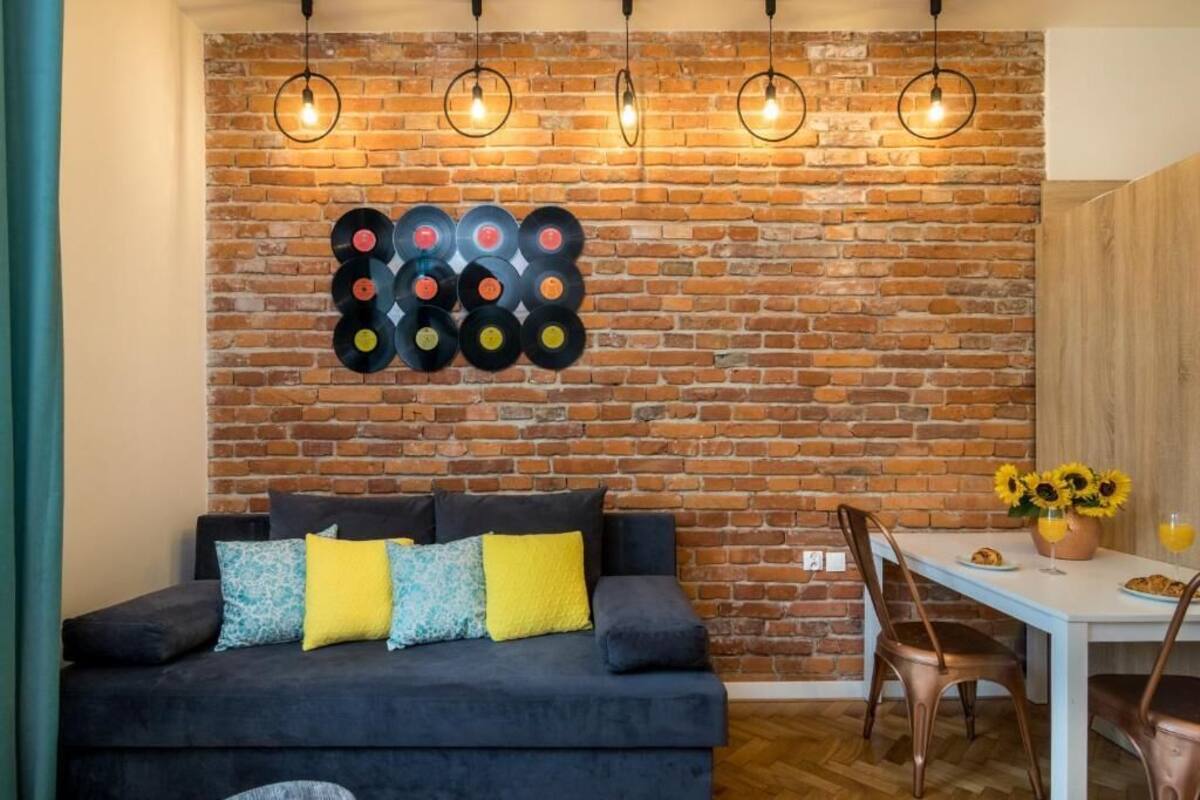 Ein gemütlicher Wohnbereich mit Backsteinwand, einer Couch mit bunten Kissen und einem Esstisch mit Stühlen.