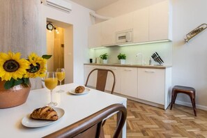 A modern kitchen with white cabinets, a microwave, and a sink. There is a dining table with a croissant and a vase of sunflowers. - Apartments Starowiślna 54  A4You (Kraków)