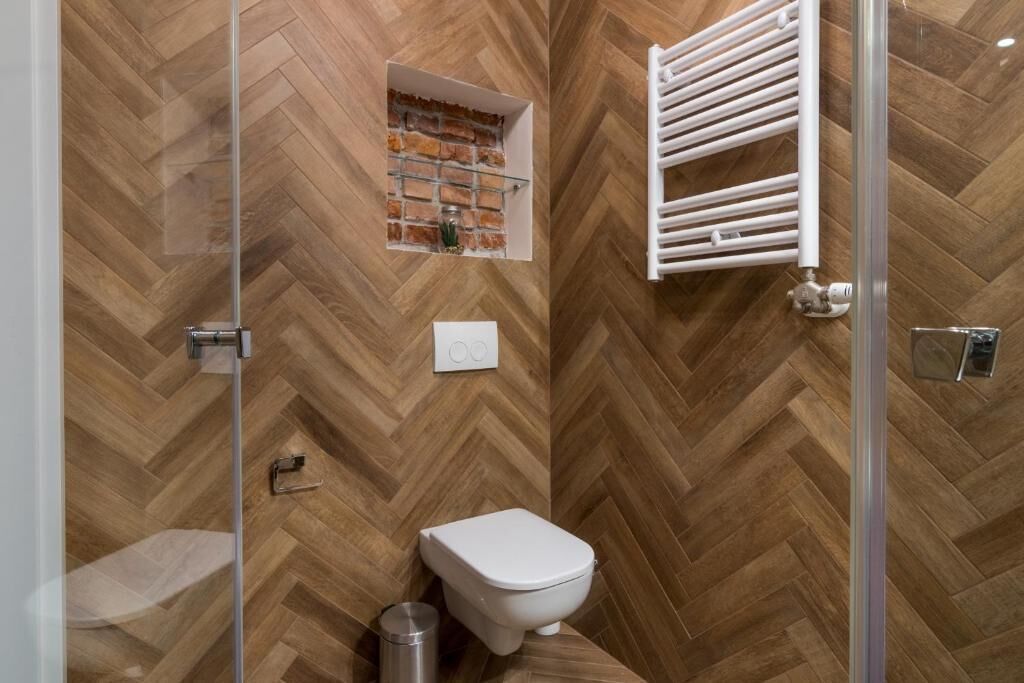 A bathroom with a herringbone wood floor, a white toilet, a glass shower enclosure, and a towel rack.