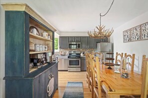 Uma cozinha com armários de madeira, uma mesa de jantar, cadeiras, um lustre e uma geladeira.