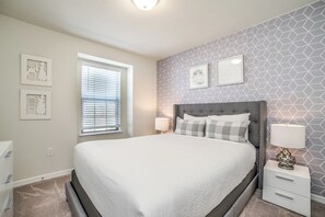 A bedroom with a large bed, bedside tables, a window with blinds, and geometric-patterned wallpaper. - Pool Oasis! 5BR Townhome w/ Patio near WDW (Kissimmee)