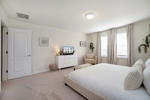 Une chambre à coucher avec un lit, une commode, une chaise et une fenêtre avec des rideaux.