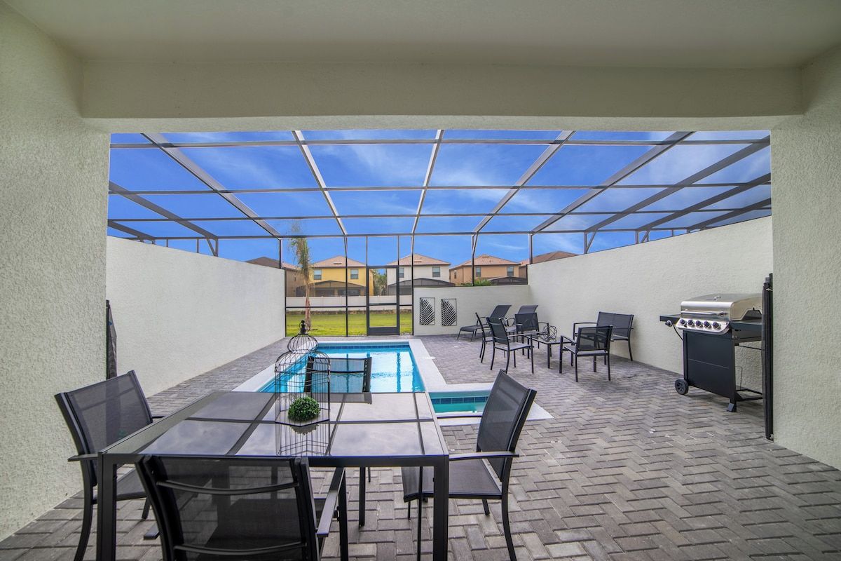 A covered patio with a pool, outdoor seating, and a grill.