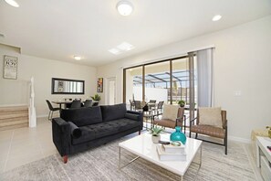A modern living room with a black sofa, a white coffee table, and a dining area with a table and chairs. - Pool Oasis! 5BR Townhome w/ Patio near WDW (Kissimmee)