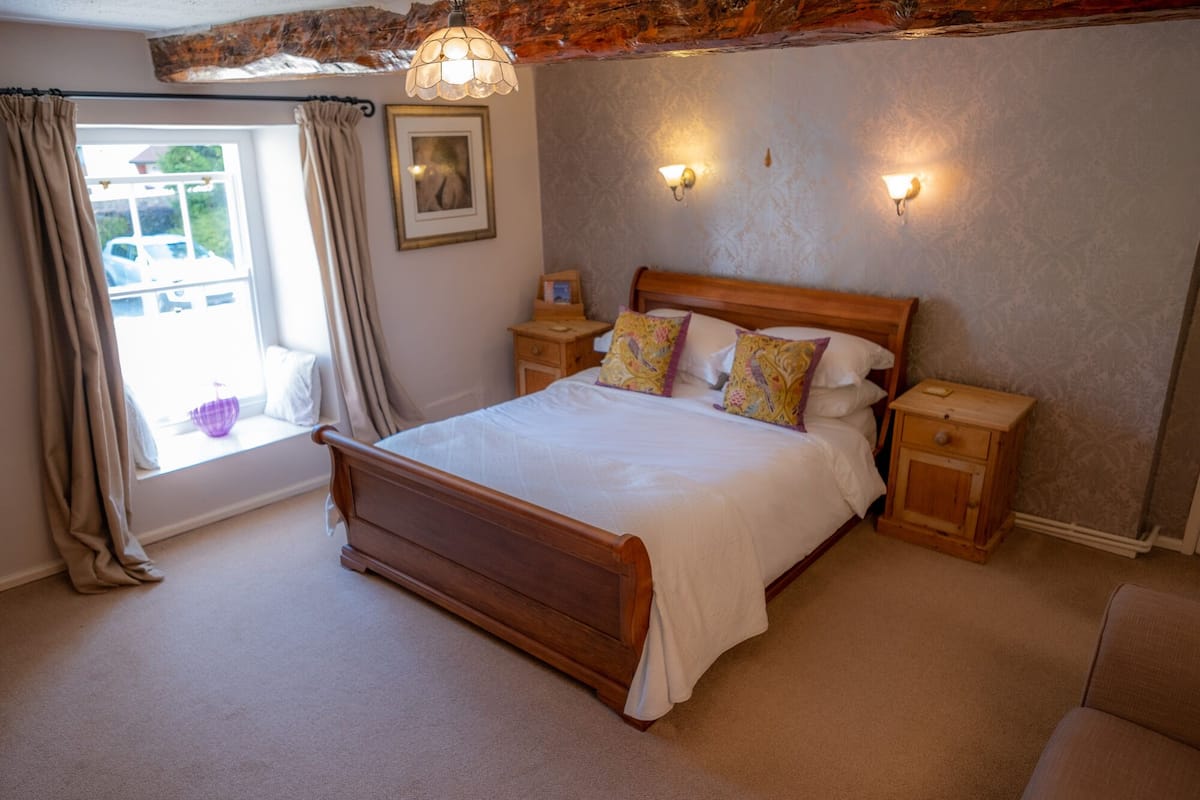 Une chambre à coucher avec un lit en bois, deux tables de chevet, une fenêtre avec des rideaux et des lampes fixées au mur.