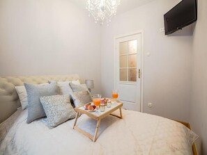 A bedroom with a bed, pillows, a bedside table, a tray with breakfast items, and a television on the wall.