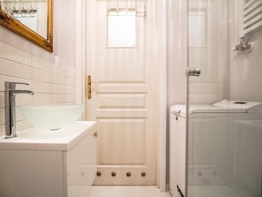 A bathroom with a white door, a glass shower enclosure, and a white sink with a modern faucet.