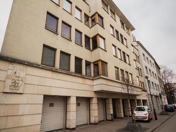 A multi-story building with a beige facade, multiple windows, and a closed garage door. - Apartment Skawińska A4You (Kraków)