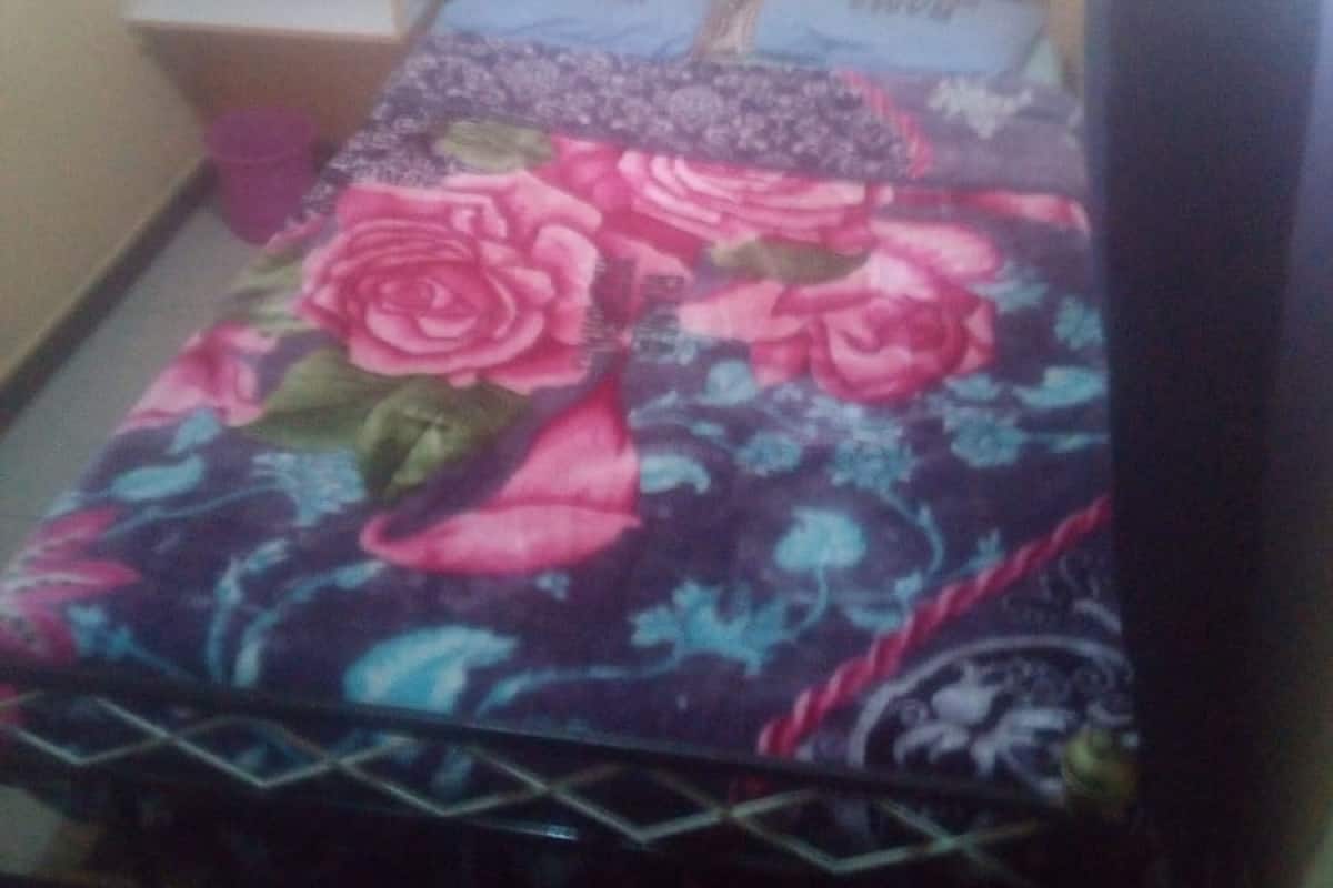 A bed with a floral bedspread, a headboard, and a nightstand with a lamp.