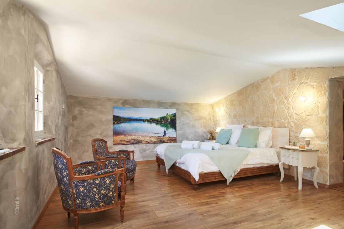 A bedroom with a large bed, a chair, a nightstand, and a wall-mounted lamp.
