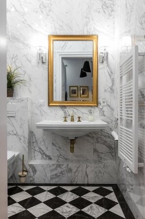 A bathroom with a marble wall, a gold-framed mirror, a white sink, and a black and white checkered floor. - Apartments Zwierzyniecka A4You (Kraków)