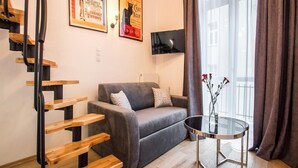 Ein modernes Wohnzimmer mit einem grauen Sofa, einem Glastisch, einer Holztreppe und zwei Postern an der Wand.