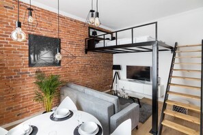 A compact living space with a loft bed, a dining area with a table set for two, and a television mounted on the wall. - Apartments Zwierzyniecka A4You (Kraków)