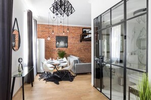 A modern kitchen with a glass enclosure, a dining area with a white table and chairs, and a brick wall with a hanging light fixture. - Apartments Zwierzyniecka A4You (Kraków)