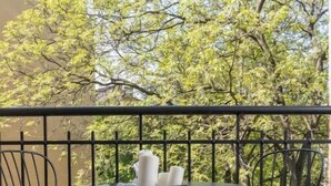 Ein Balkon mit Schachbrettmuster-Boden, zwei Tischen und Stühlen, umgeben von Grünpflanzen und einem Gebäude.