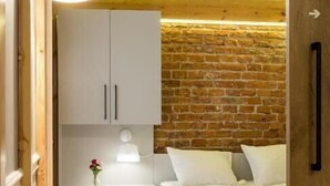 Ein Schlafzimmer mit Holzbalkendecke, einer Backsteinwand, einem weißen Bett, einem Nachttisch und einer Lampe.