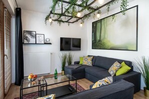 Uma sala de estar moderna com um sofá seccional, uma mesa de centro de vidro e uma grande pintura de uma floresta.