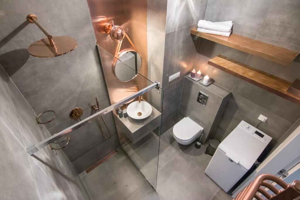 Ein modernes Badezimmer mit einer Duschkabine, einem runden Spiegel, einem Waschbecken, einer Toilette und einer integrierten Waschmaschine.