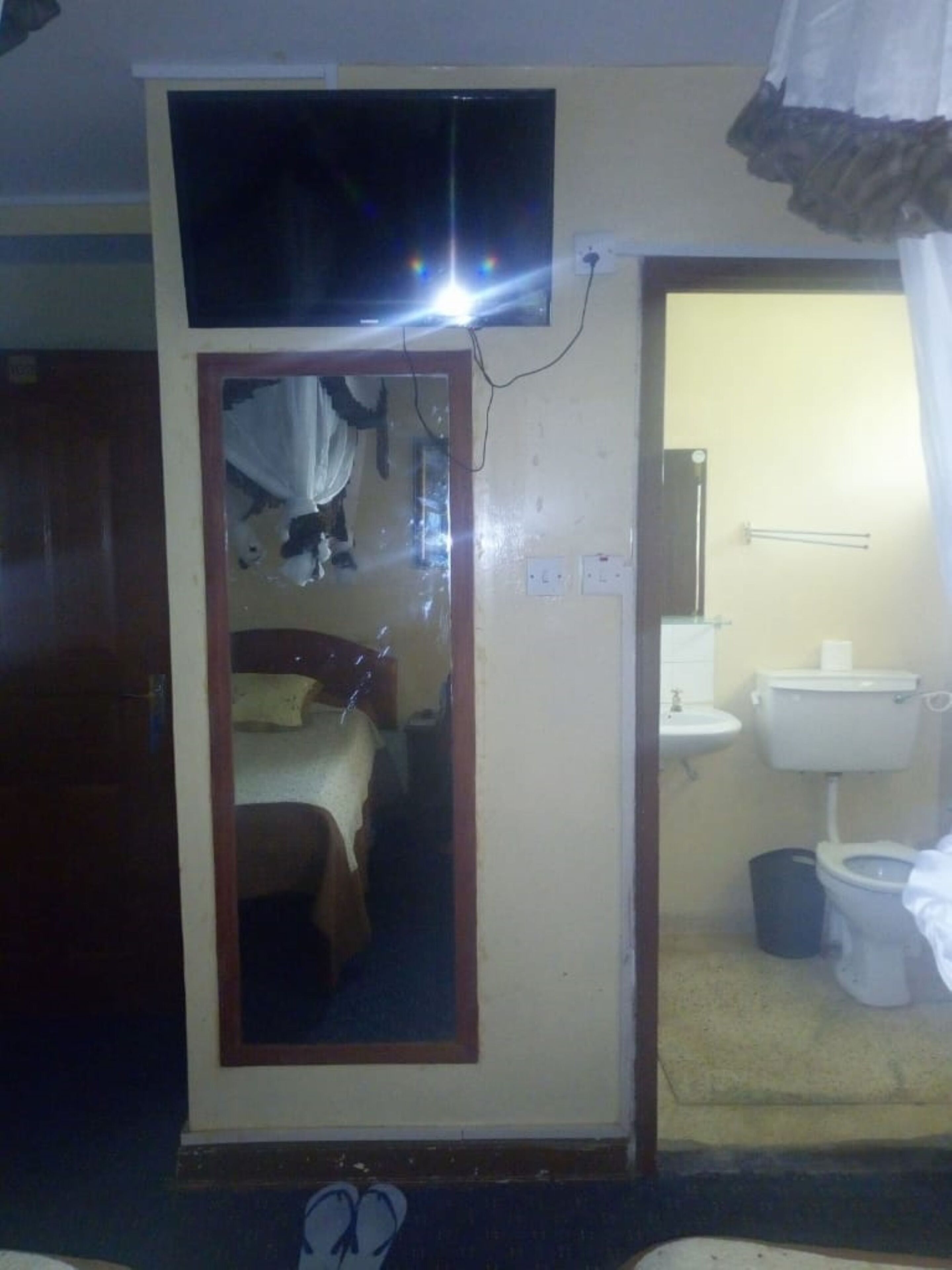 Una habitación con una cama, un televisor montado en la pared y un baño con inodoro y lavabo.