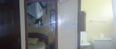 Una habitación con una cama, un televisor montado en la pared y un baño con inodoro y lavabo.