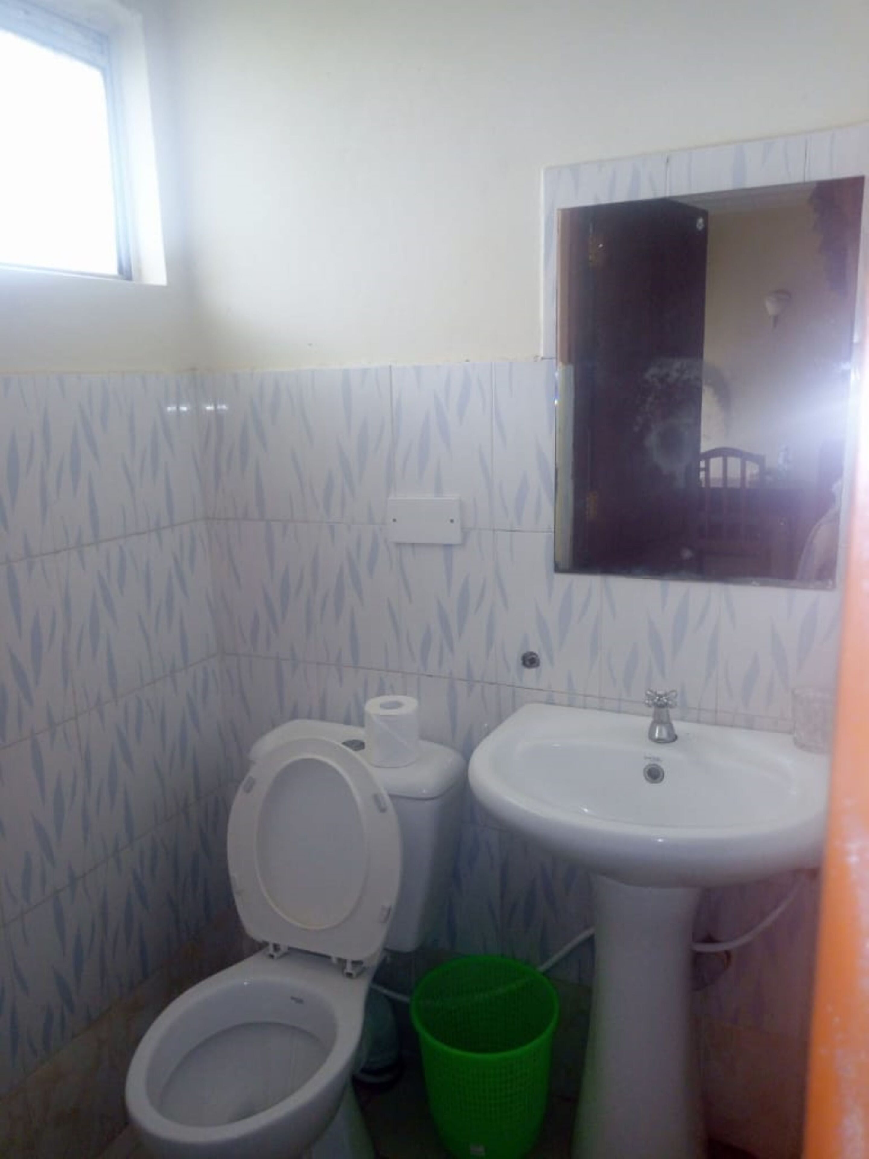 A small bathroom with a toilet, sink, and a green trash bin.