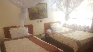A hotel room with two beds, a nightstand, a wall clock, and a painting of a cheetah. - Homa Bay Tourist Hotel (Homa Bay)