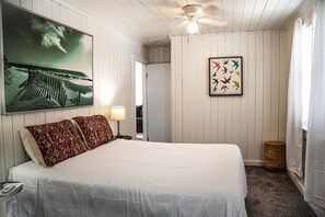 Un dormitorio con cama, un cuadro colgado en la pared, ventilador de techo y una obra de arte enmarco.