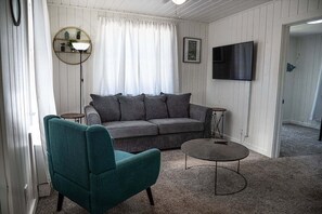 A living room with a grey sofa, teal armchair, round coffee table, and a TV mounted on the wall.
