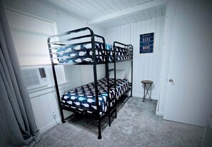 A bunk bed room with a 'Ride the Wave' sign, a small table, and a window with blinds.