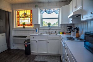 Una cocina con armarios blancos, una estufa, un lavamanos y un ventanal con vistas, además de un vitral.