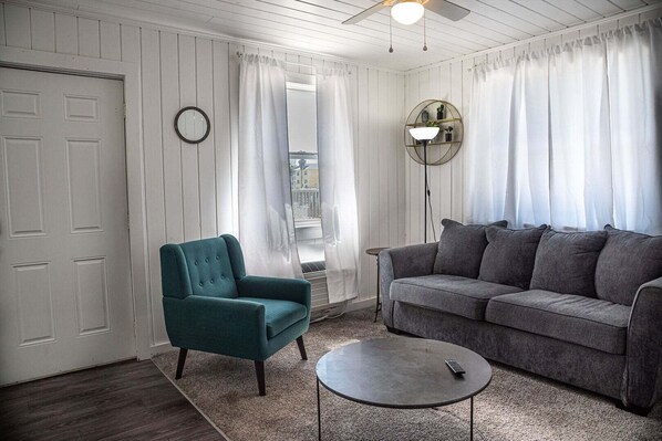 A living room with a teal armchair, a gray sofa, a round coffee table, and a ceiling fan.
