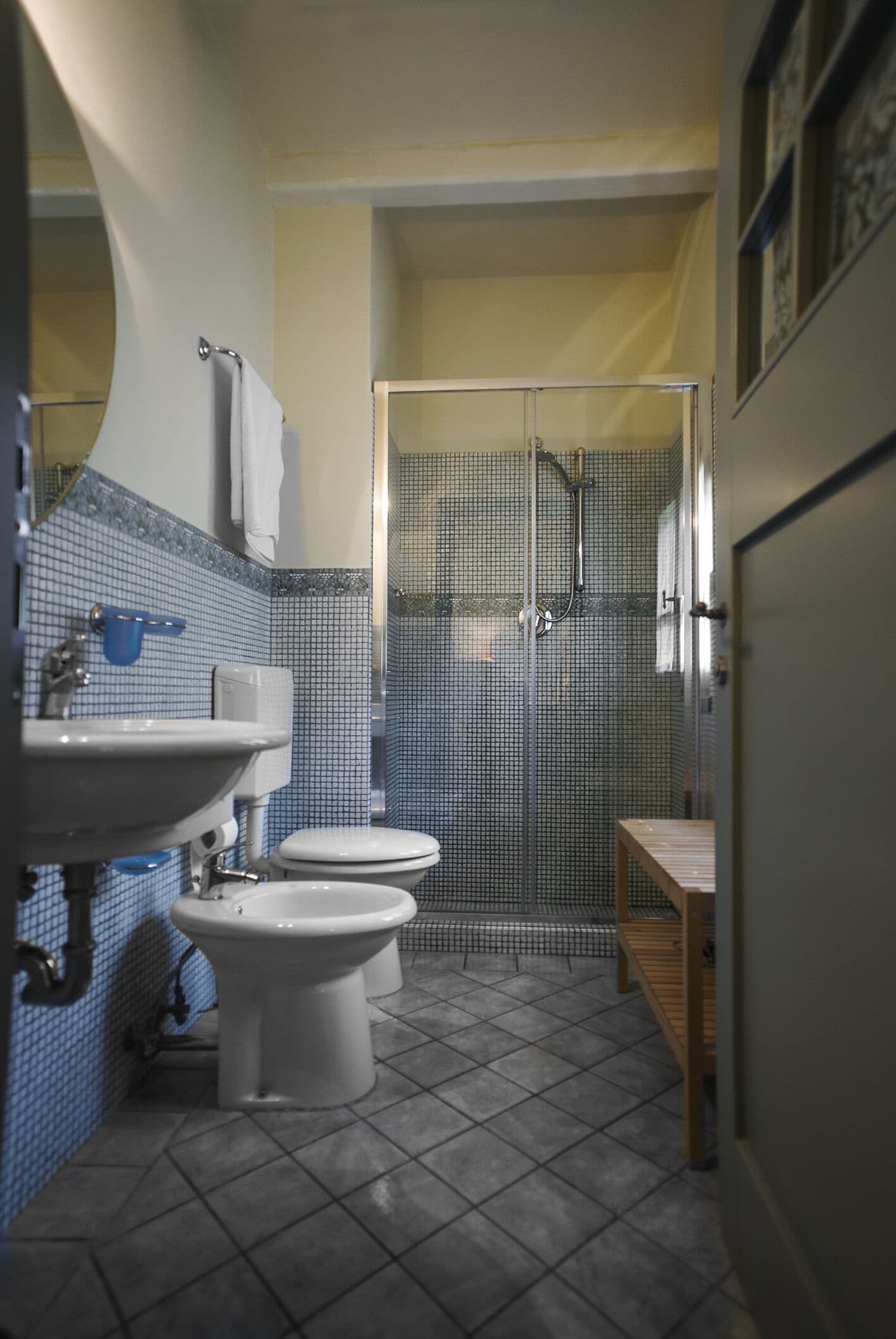 A bathroom with a sink, two toilets, a shower, and a tiled floor.